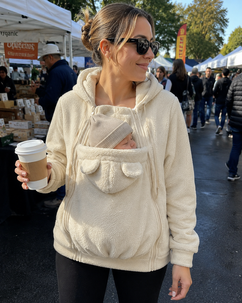 Mom at farmers market holding coffee, baby asleep in cream Snoozeroo pouch hoodie