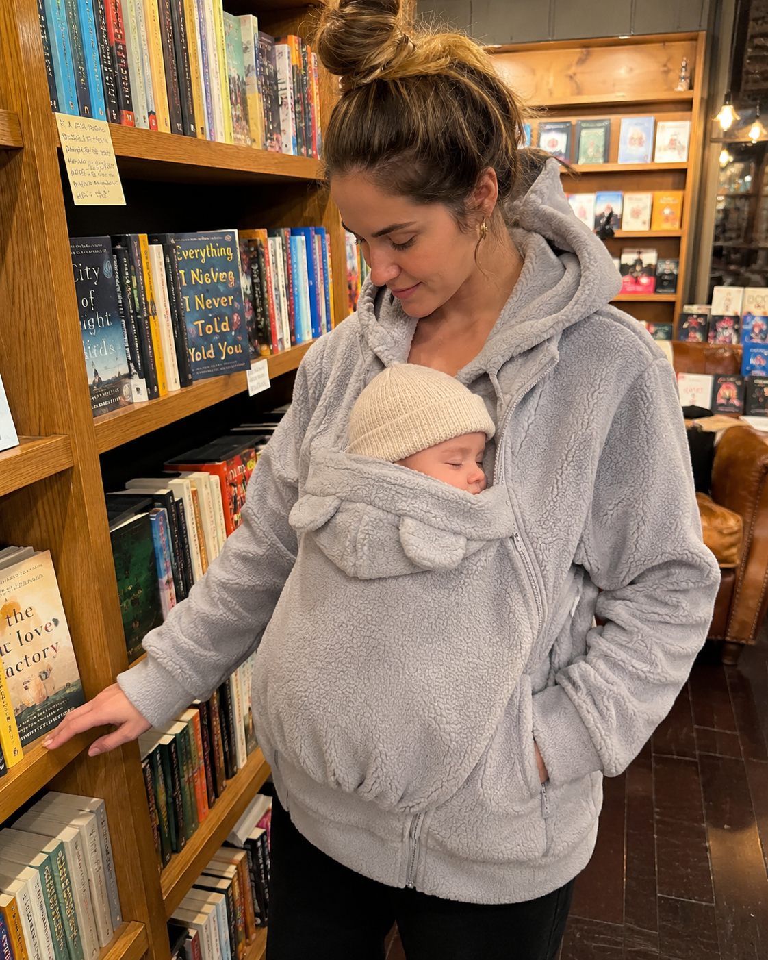 Mom browsing bookstore with baby sleeping in grey Snoozeroo fleece pouch